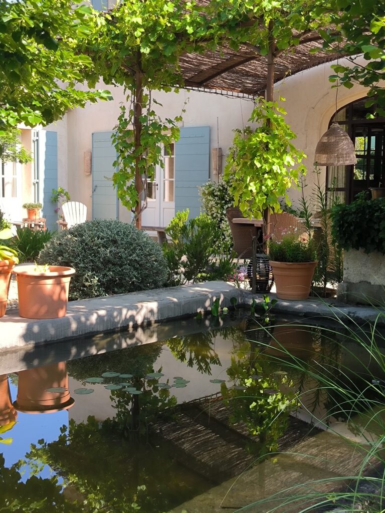 Une terrasse avec des plantes en pot, de l’ombre et un petit bassin