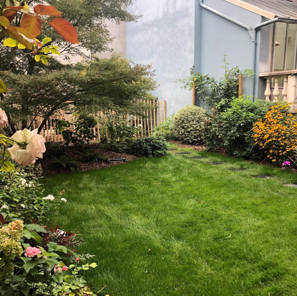 Jardin avec massifs fleuris et pelouse contre un mur